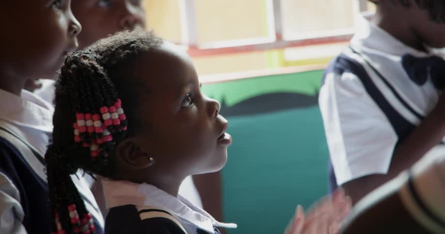 Children in school uniforms clap and sing