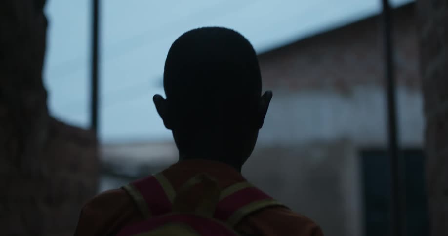 A child with a backpack walks next to buildings