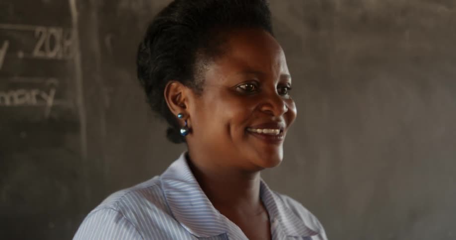 Woman smiles while standing in front of a blackboard