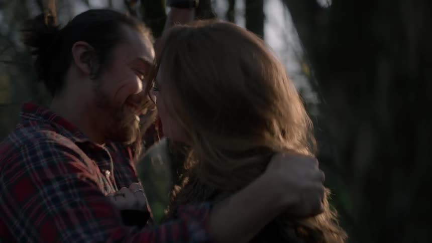 A man and woman embrace and laugh in a wooded area