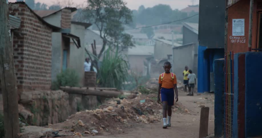 Boy wearing backpack walking on dirt path in foreign town