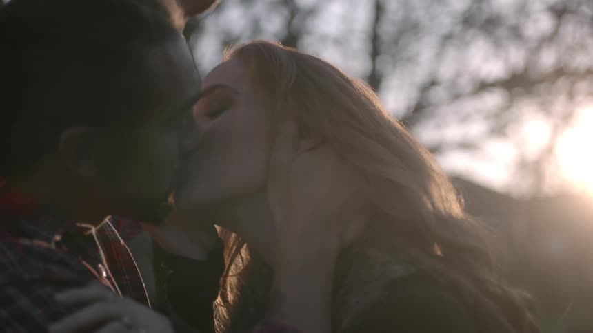 A man and a woman kiss in a wooded area