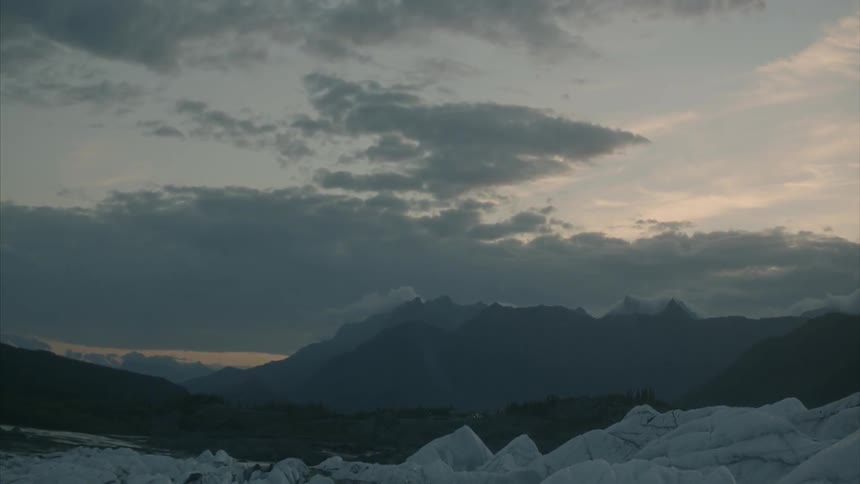 Snow on ground in front of mountains on cloudy evening