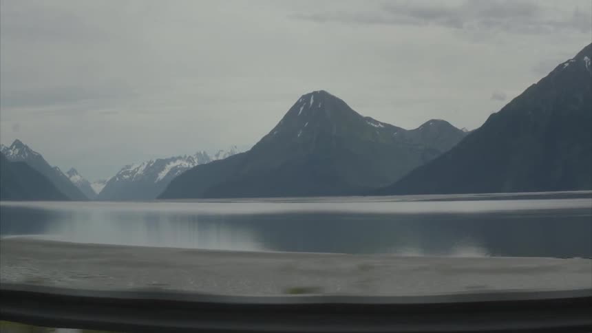 Mountains and a lake can be seen over the road's guardrail