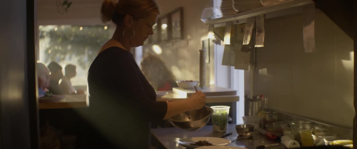 A woman dishes out food onto plates in a restaurant kitchen