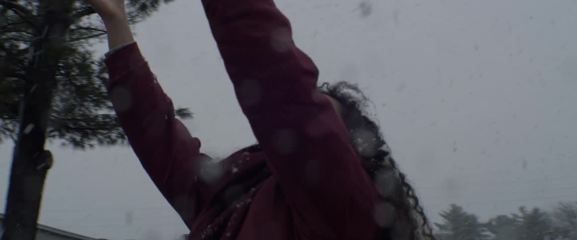 A woman is looking up at the snow sticking her tongue out as it falls