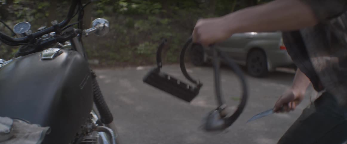 Man removing part from motorcycle with knife in driveway