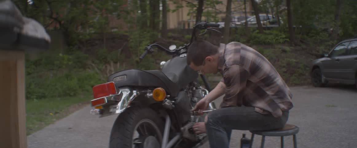 A man is sitting down to work on his motorcycle