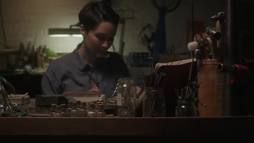 A woman is working with tools inside of a dark shop