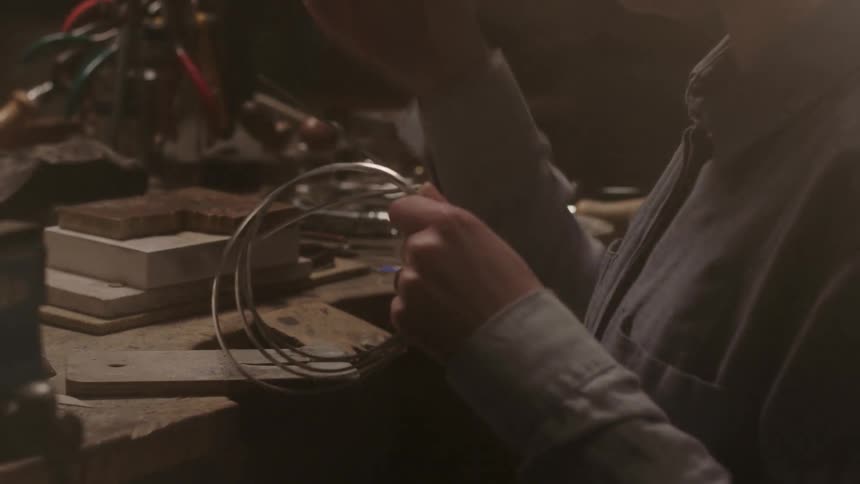 A person picks up a roll of solder metal and clips a piece