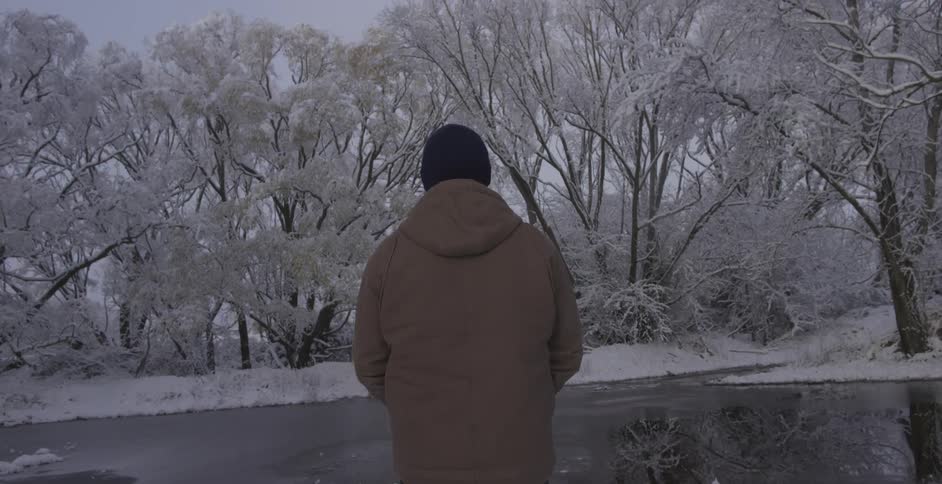 A man standing next to a frozen lake and snow-covered trees
