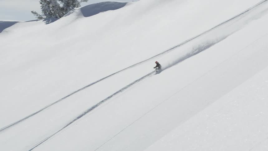 A skier launches into the air over a ledge and lands on the hillside below
