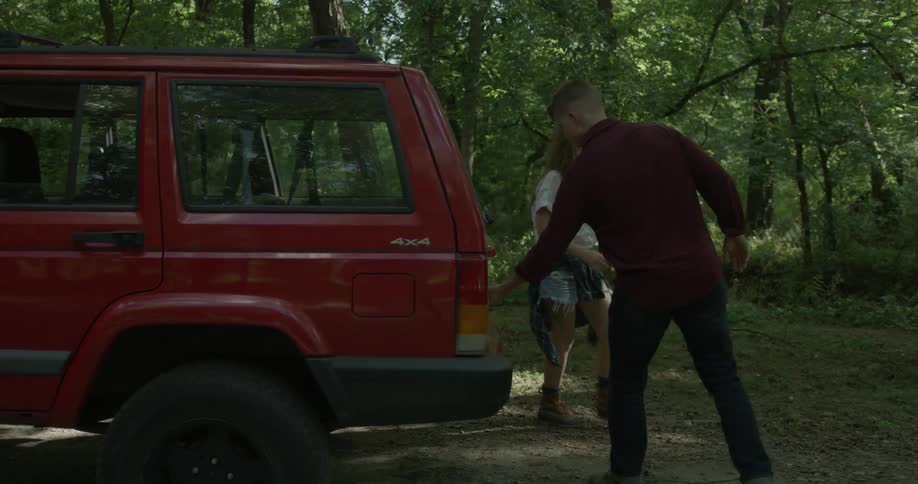 A man and woman walk to the back of an suv and lift the tailgate