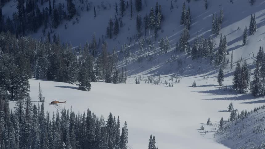 A helicopter sits on a snow covered mountain clearing