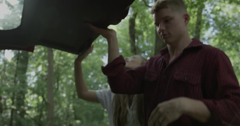 A man and woman remove camping gear from the back of a vehicle in the woods