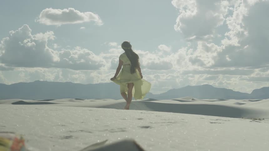 Woman wearing a yellow dress walks barefoot in the desert