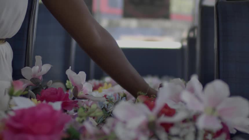 A woman sits in a bus with flowers filling the aisle