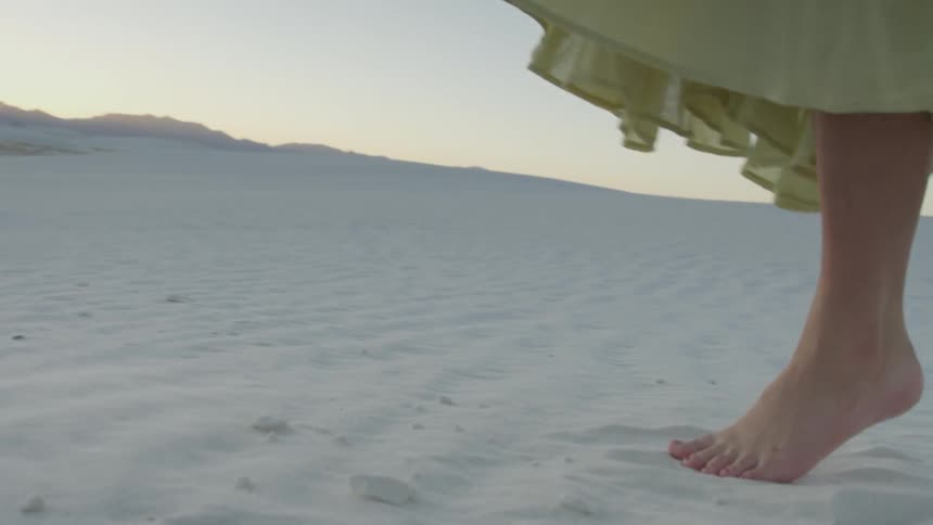 A woman tiptoes and kicks up her feet in the sand
