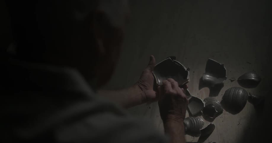 A person picks up the pieces of the vase