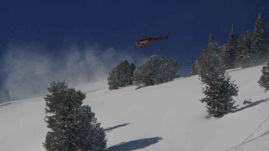 A helicopter kicks up a cloud of snow as it rises above a hillside