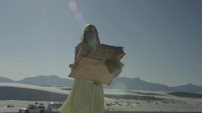 A woman walking on sand is carrying a canvas and cushion