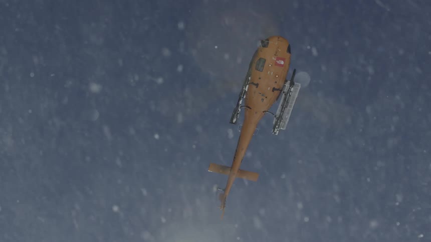 A yellow helicopter floats in the air above