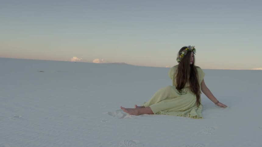 A woman wears a flower wreath while sitting alone in a desert