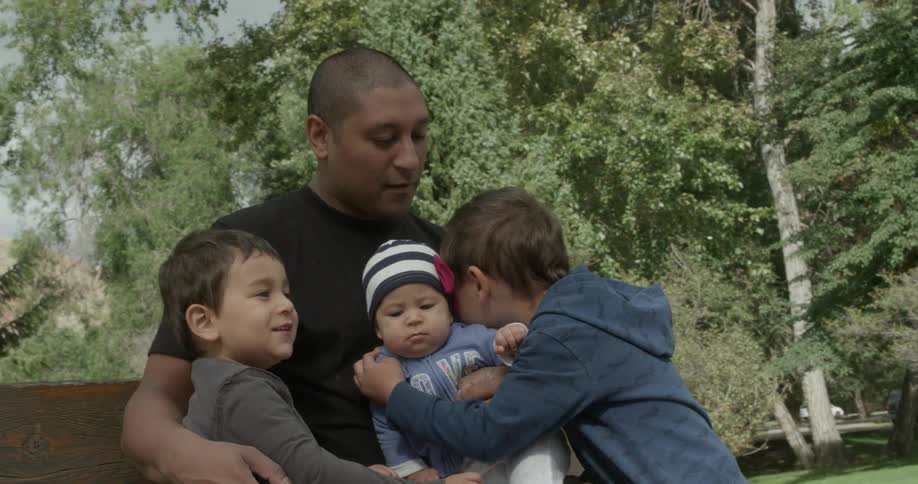 Man and three kids sit on a bench together in a park
