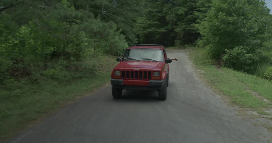 A red vehicle drives down a wooded road