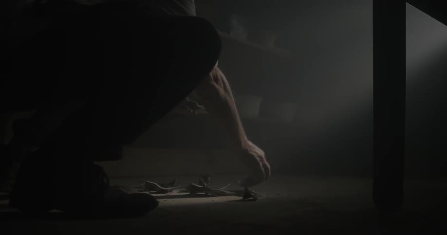 Man picking up pieces of broken scraps in dim and dusty room