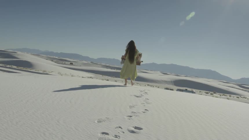 A woman in a dress walks in the desert