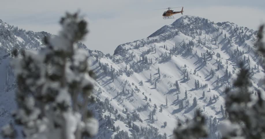 A helicopter flies over snowy mountains