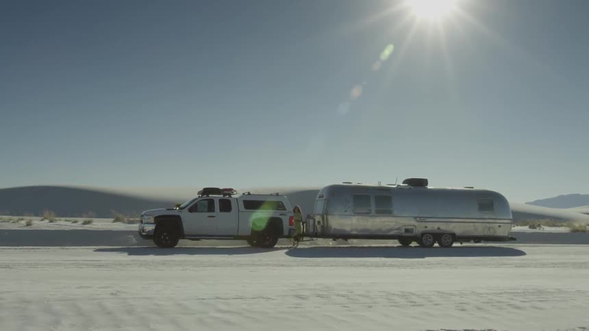 A person is standing next to a truck and camper in the middle of the desert