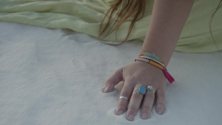 A woman's hand rests in the sand as she sits still