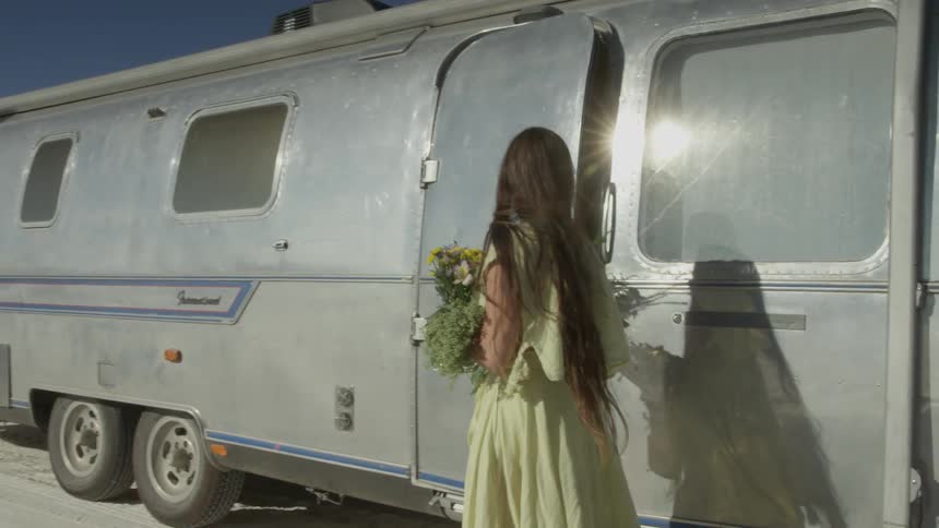 Woman holding flowers stepping out of motorhome in sandy wilderness
