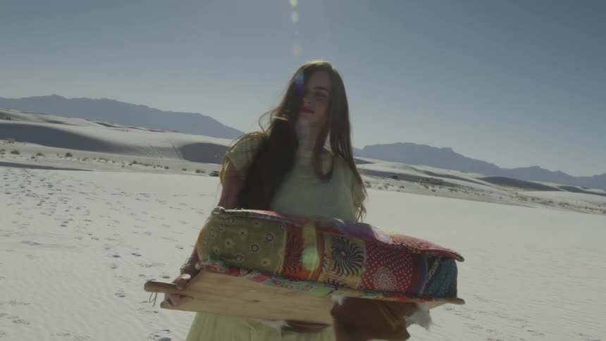 A woman carries pillows in the desert