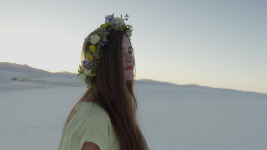 A woman with a flower wreath on her head walks in the desert