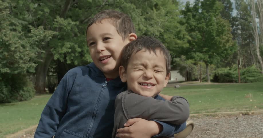 Two boys hug each other outside in a yard