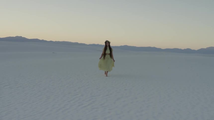 A woman flounces her skirt as she walks over white sands