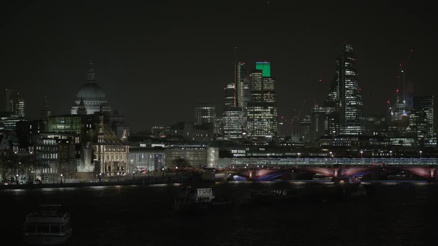 A boat sails towards the city at night