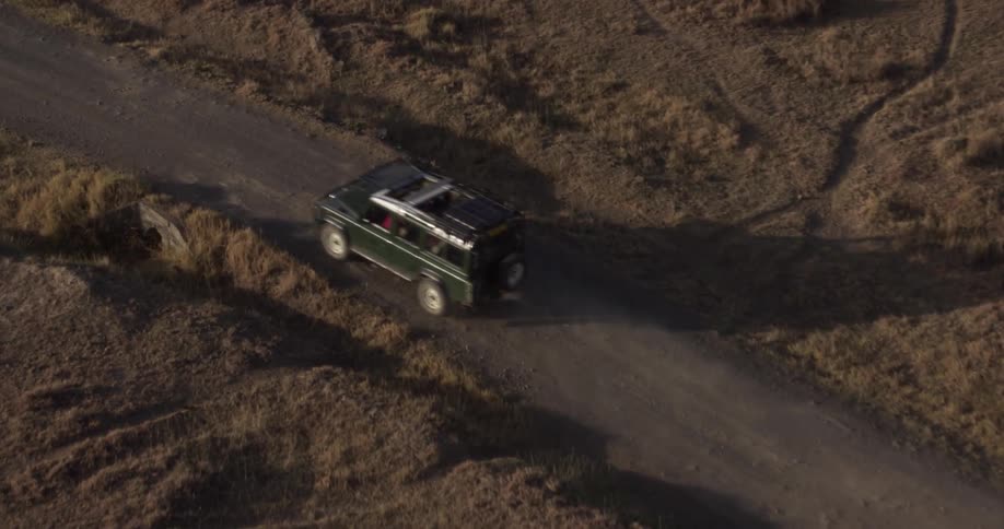 Jeep drives down a dusty road at sunset