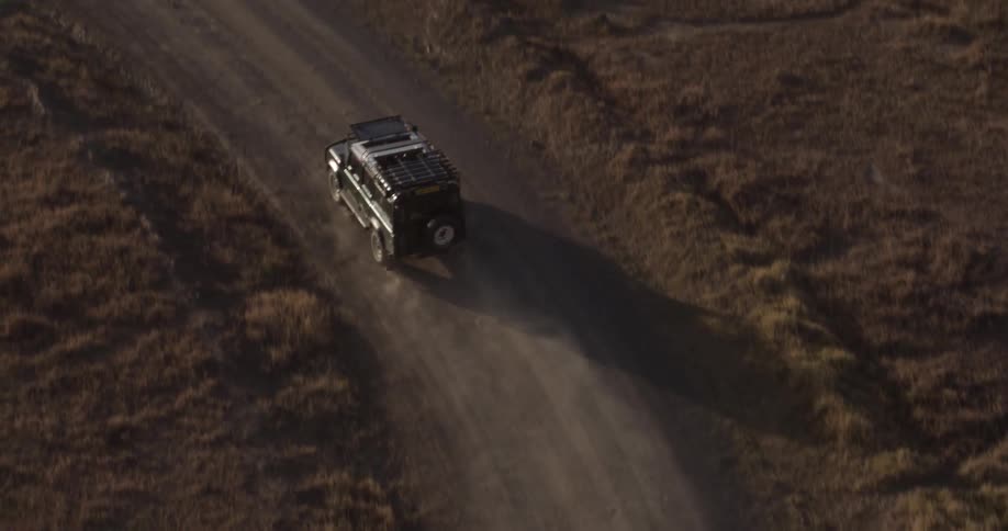 Jeep drives down a dusty road at sunset