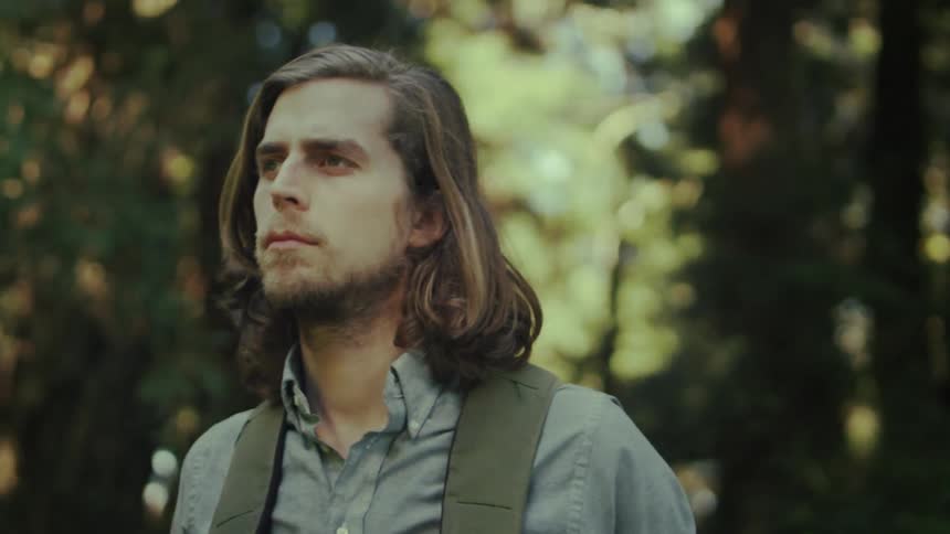 A man is hiking in the woods and takes a break