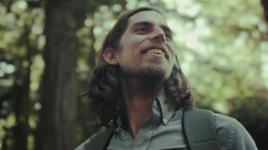 A man smiles while hiking in a forest