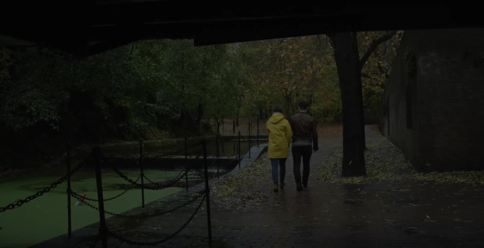 A man and woman hold hands while walking outside on a rainy day