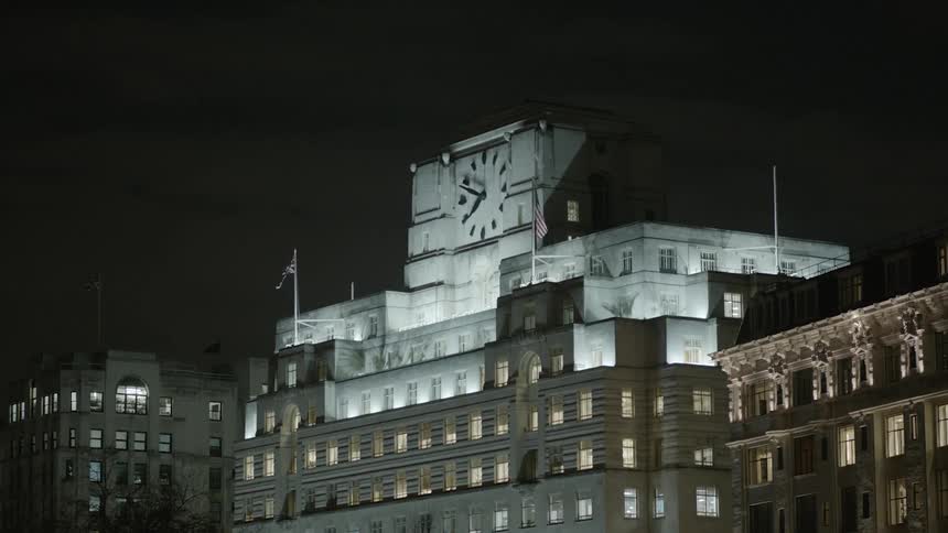 A large building with a big clock is being filmed at night