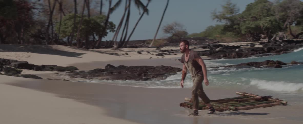 Man standing in water on a beach walks away from his raft