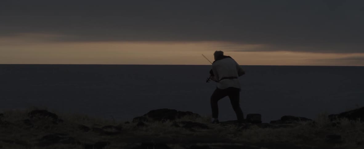 Person plays violin on a cliff next to water