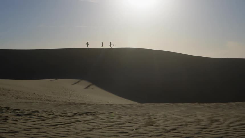 People walk across a sand dune