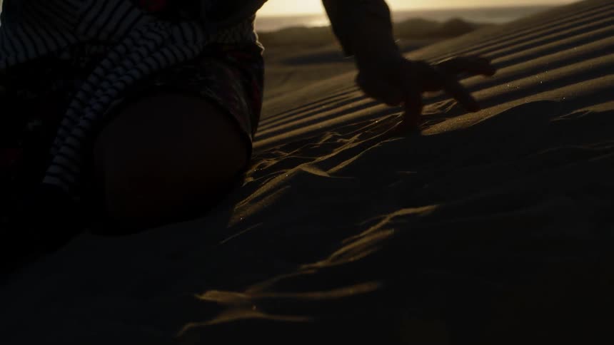 A person draws in the sand with their finger at sunset